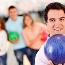 Man bowling with friends holding a ball and smiling